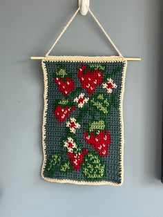 a crocheted wall hanging with flowers and leaves in green, red and white