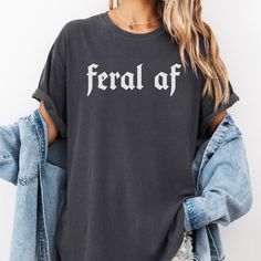 This Comfort Colors Feral AF Unisex T-Shirt is packed with attitude in minimalistic way!  Whether you're treating yourself, or gifting it to someone you love, this will quickly become your go-to tshirt! **Please size up if you are looking for the oversized t-shirt look! This is a unisex fit and runs true to size. For a better idea, please refer to the size chart in the pictures.** - Made 100% with ring-spun cotton. The soft-washed, garment-dyed fabric brings extra coziness to your wardrobe while Band Merch Cotton Tops With Funny Text, Cotton Band Merch Top With Funny Text, Edgy Cotton Shirt With Text Print, Cotton Grunge Slogan Tops, Grunge Cotton Slogan Tops, Edgy Cotton Tops With Text Print, Spring Grunge Letter Print Shirt, Edgy Cotton Slogan Tops, Grunge Cotton Shirt With Letter Print