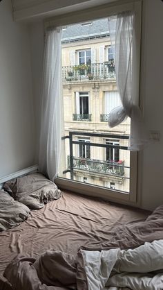 an unmade bed sitting in front of a window next to a balcony with balconies