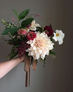 a bouquet of flowers is being held up by someone's hand with brown ribbon