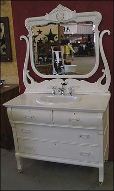 a white dresser with a mirror above it and drawers below the sink, in front of a red wall