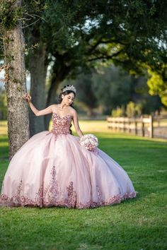 a woman in a pink dress standing next to a tree and wearing a tiara