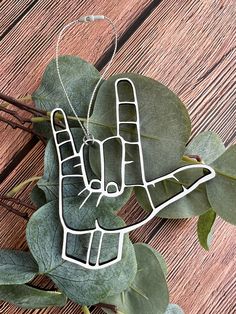 a metal peace sign hanging from a leafy plant on a wooden table with leaves