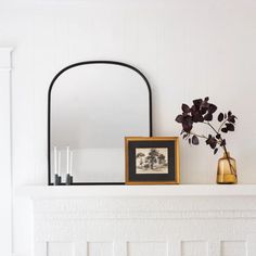 a white fireplace with a mirror, vase and candles on the mantel above it