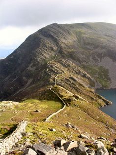 a mountain with a path going up the side of it next to a body of water