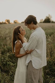 a man and woman standing together in a field with tall grass, looking at each other