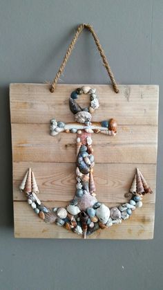 an anchor made out of seashells and rope hangs on a wooden sign with string