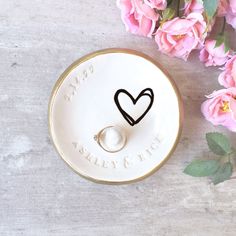 a wedding ring holder with a heart on it and pink flowers in the foreground