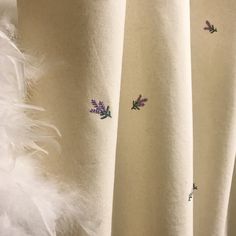 the curtains are decorated with purple flowers and white feathers in front of an off - white background