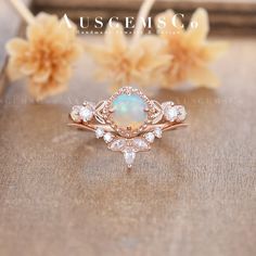 an opal and diamond ring sitting on top of a wooden table next to flowers