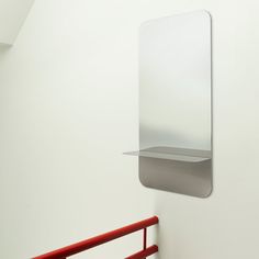 a mirror hanging on the wall next to a red hand rail in a white room