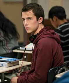 a young man sitting at a desk with headphones on his ears and looking off to the side