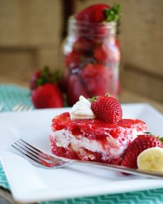 a piece of strawberry cheesecake on a white plate with a fork and mason jar in the background