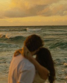 a man and woman embracing on the beach with waves crashing in the background at sunset