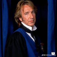 a man with long hair wearing a blue robe and standing in front of a curtain