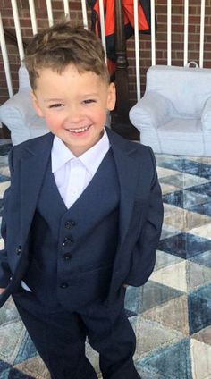 a young boy in a suit and tie standing on a rug with his hands in his pockets