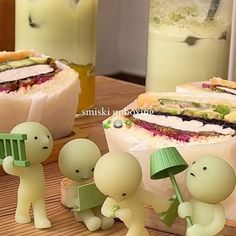 three small plastic figurines sitting on top of a wooden table next to sandwiches