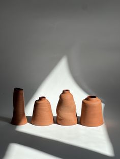 three clay vases sitting on top of a white table next to each other in front of a shadow