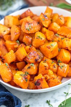 a white bowl filled with cooked carrots on top of a marble counter next to a blue towel