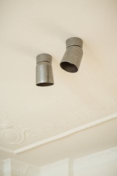 two metal cups hanging from the ceiling in a room with white walls and plaster molding