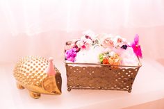 a hedgehog toy next to a basket full of flowers on a white tablecloth