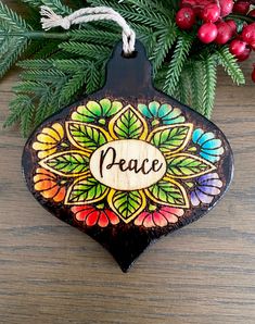 a wooden ornament with the word peace painted on it next to christmas tree branches