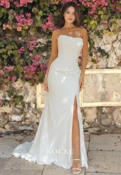 a woman wearing a white dress standing in front of a wall with flowers on it