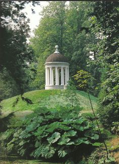 a white gazebo sitting on top of a lush green hillside surrounded by trees and bushes