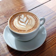 a cappuccino on a white saucer sitting on top of a wooden table