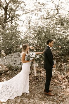 a bride and groom standing in the woods holding hands with each other as they look at each other