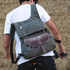 a man with a backpack on his back riding a bike in front of some dry grass