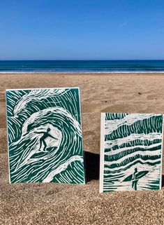 two green and white paintings sitting on top of a sandy beach