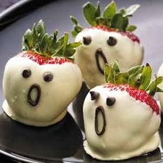 four white chocolate covered strawberries with faces drawn on them, sitting on a black plate