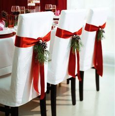 the chairs are covered with red ribbon and decorated with pinecone sprigs