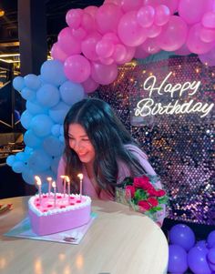 a woman sitting at a table with a birthday cake and balloons in front of her