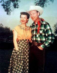 a man and woman standing next to each other in front of a tree wearing cowboy hats