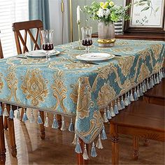 a dining room table covered in a blue and gold damask cloth with tassels