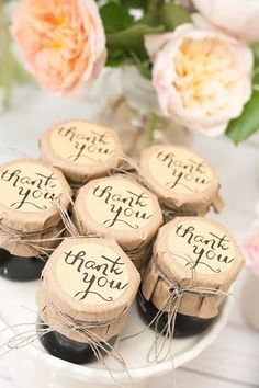 there are six wine corks with the words thank you on them and some flowers in the background