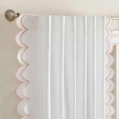 a white curtain with pink scalloped trim hanging on a wall next to a window