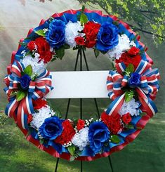 a wreath with red, white and blue flowers on it sitting in front of a tree