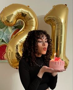 a woman holding a cake with candles in front of her face and number two balloons behind her