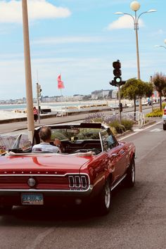 a red convertible car driving down a street next to a traffic light on a sunny day