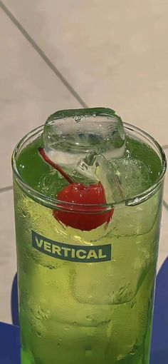 a green beverage with a red cherry on the rim and ice in it, sitting on a blue table