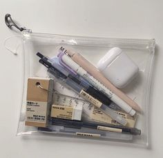 an assortment of pens and pencils in a clear plastic bag on a white surface