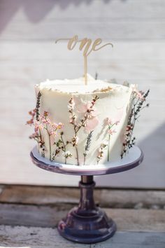 a white cake with pink flowers and the word one on top is sitting on a plate