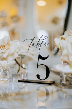 the table numbers are placed on clear acrylic plates with white flowers in vases