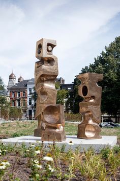 three sculptures are in the middle of a field with buildings in the backgroud