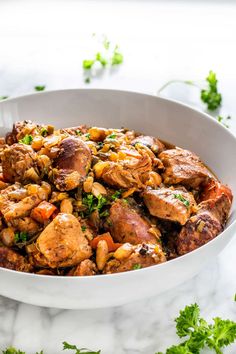 a white bowl filled with meat and vegetables on top of a marble counter next to parsley