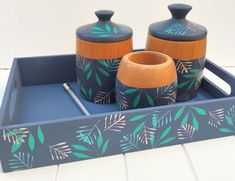 two ceramic jars and a pen on a tray with leaves painted on the sides,