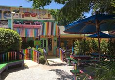 the colorful building has many tables and umbrellas in it's front garden area